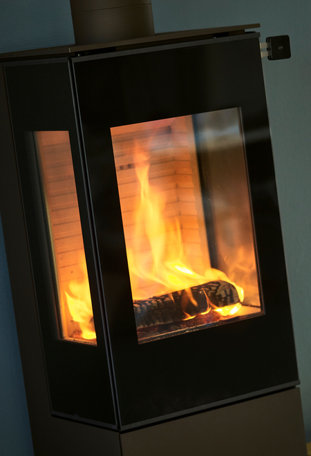 Holz-Kaminofen NEXO 120 in Schwarz mit Vollglas-Feuerraumtür und zwei Seitenfenstern, mit direktem Blick auf das brennende Feuer